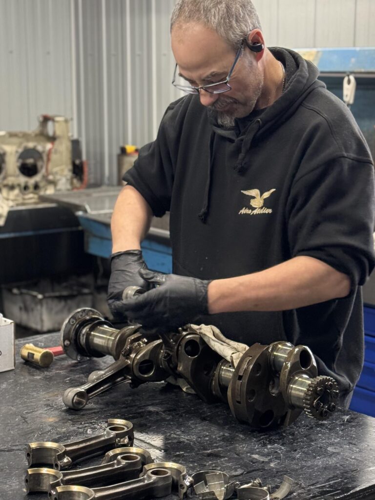 La photo montre un technicien spécialisé retirant méthodiquement les connecting rods d'un crankshaft Lycoming sur un banc de travail.